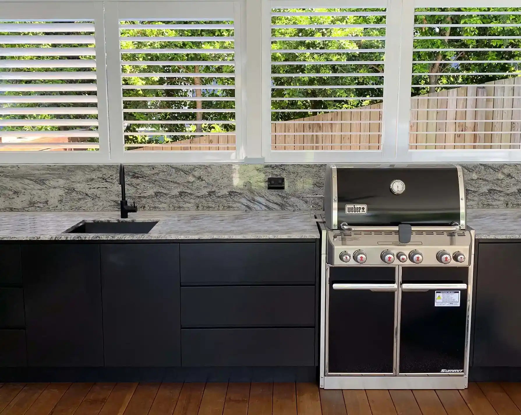 Outdoor patio with black cabinetry, built-in BBQ, and white aluminium shutters for all-season use