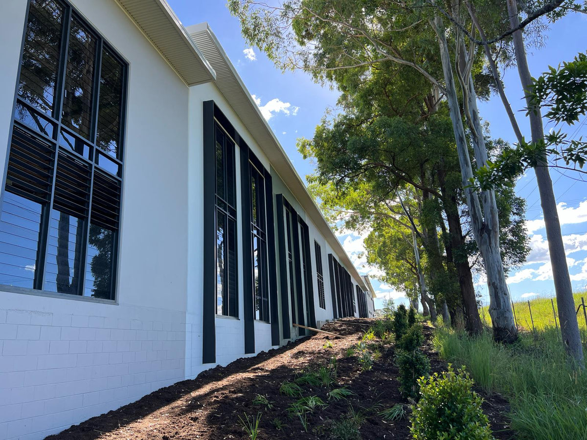White building with black window shrouds surrounded by trees and greenery