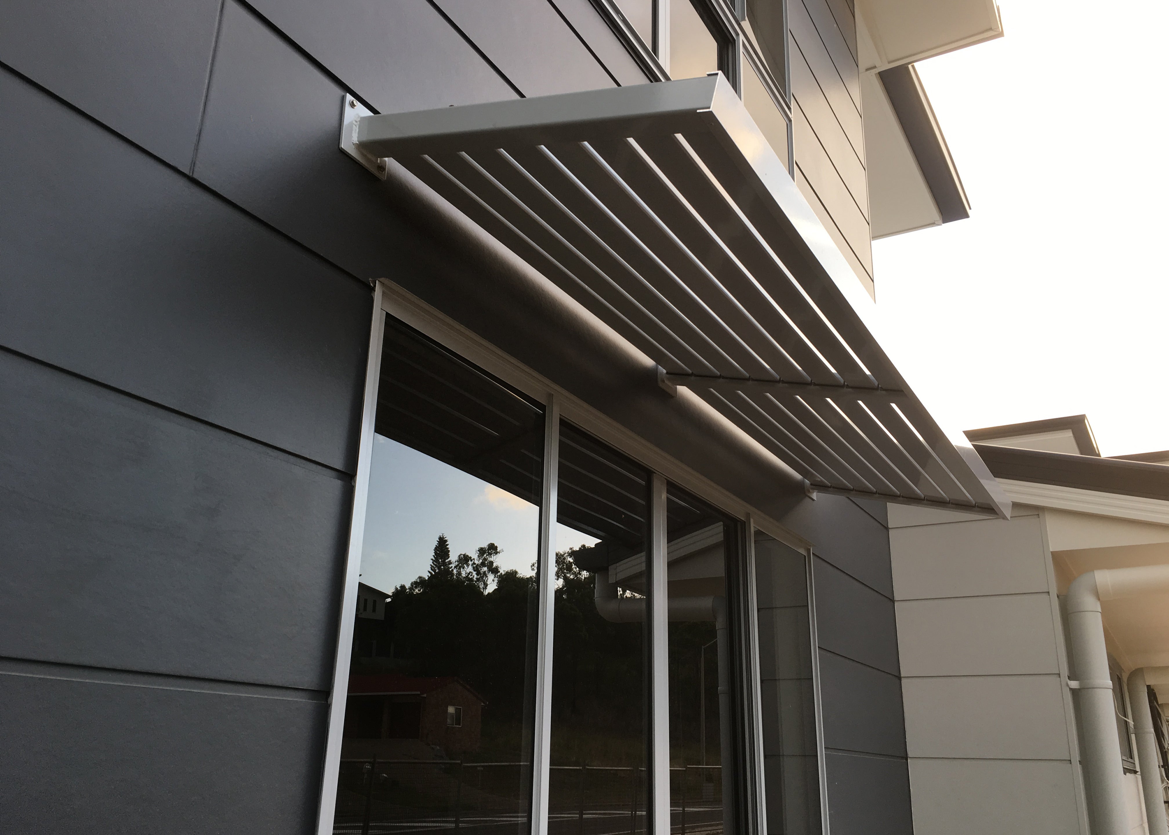 Clik'n'Fit® Aluminium Slat Awning in Dune on an angle above a large residential window.
